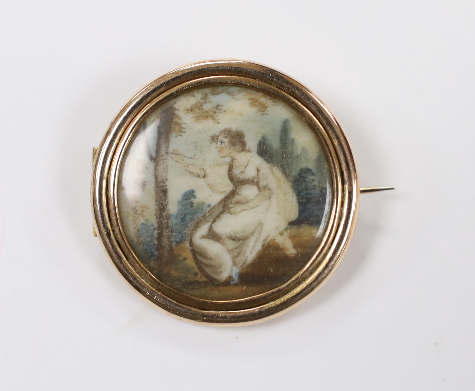 A 19th century yellow metal mounted circular brooch, with glazed back and inset miniature watercolour on ivory, depicting a lady in woodland scene, 31mm. CITES Submission reference, E5G6FZPZ